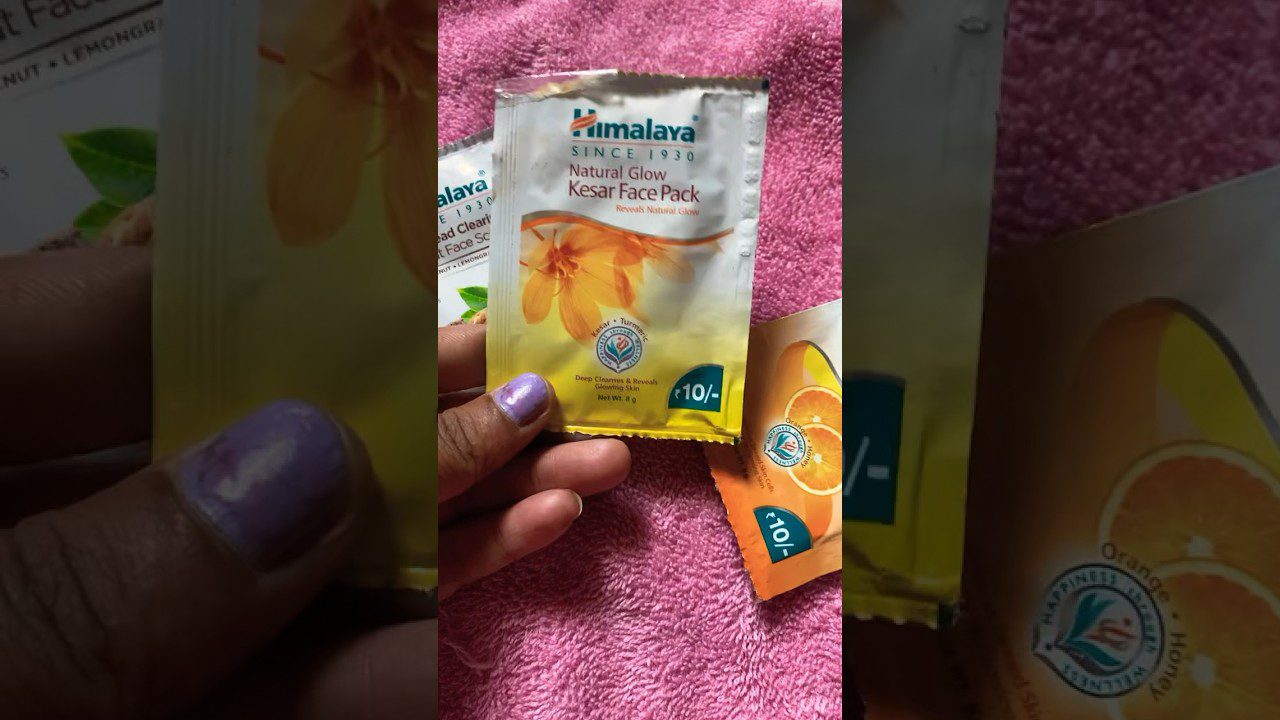 Rankoje laikomas Himalaya „Natural Glow Kesar Face Pack“ vienkartinis pakuotės maišelis ant rožinės rankšluosčio