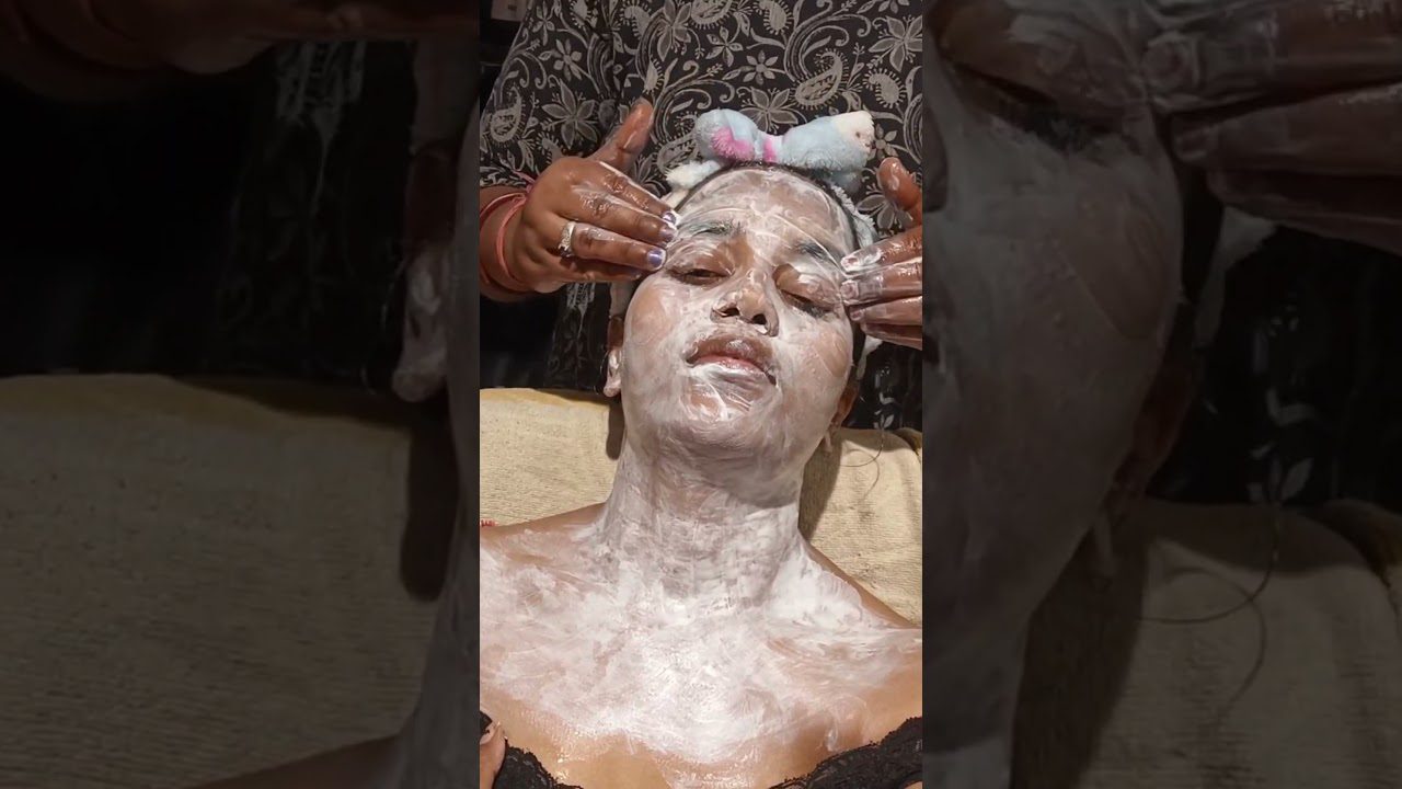 Moteris gulinti su veido ir kaklo kauke, kosmetikė masažuoja jos veidą.