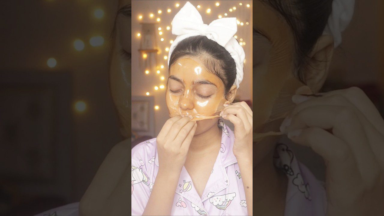 moteris su balta galvos juosta lupasi auksinę veido kaukę, dėvi rausvus pižamos marškinius