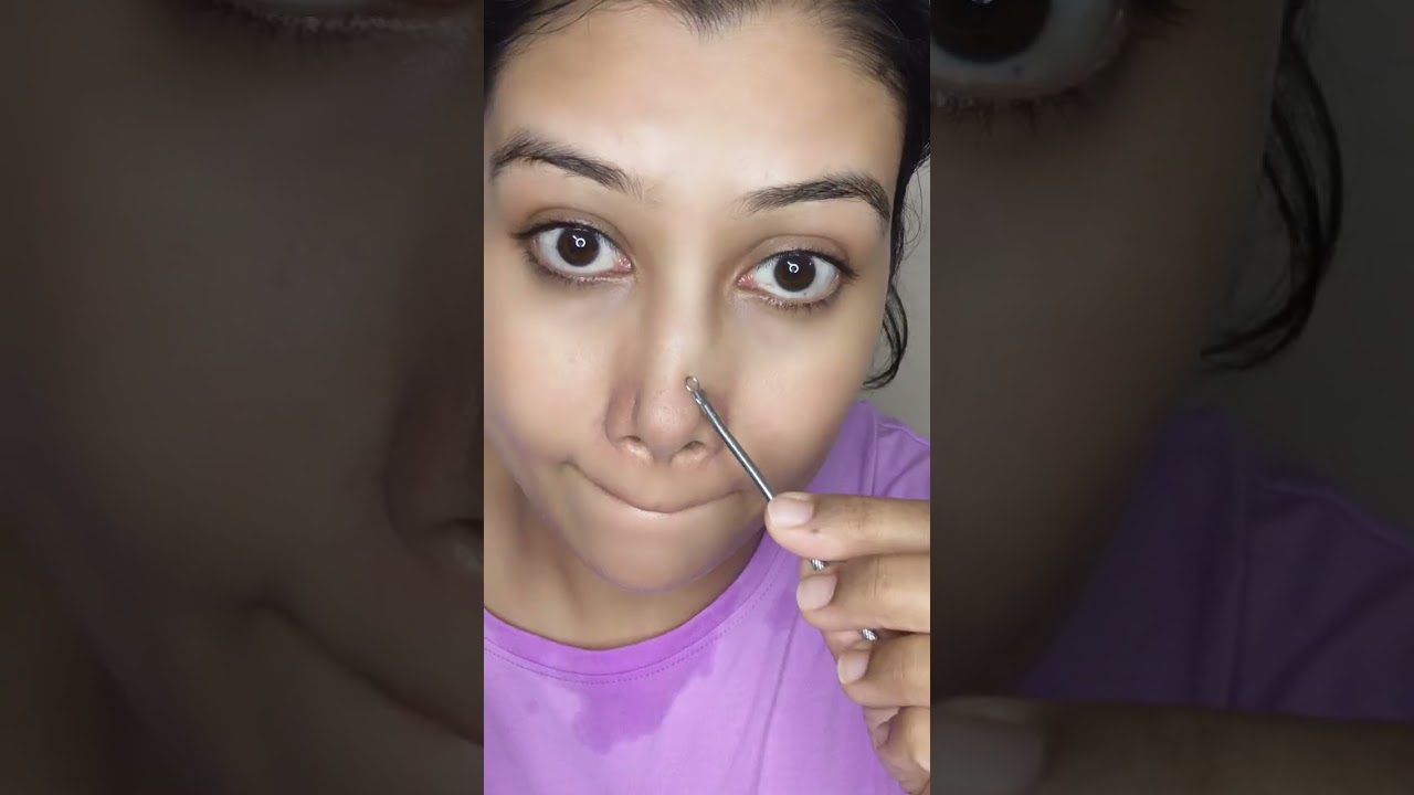 moteris naudoja spuogų spaustuvą prie nosies, rankoje laikoma metalinė priemonė