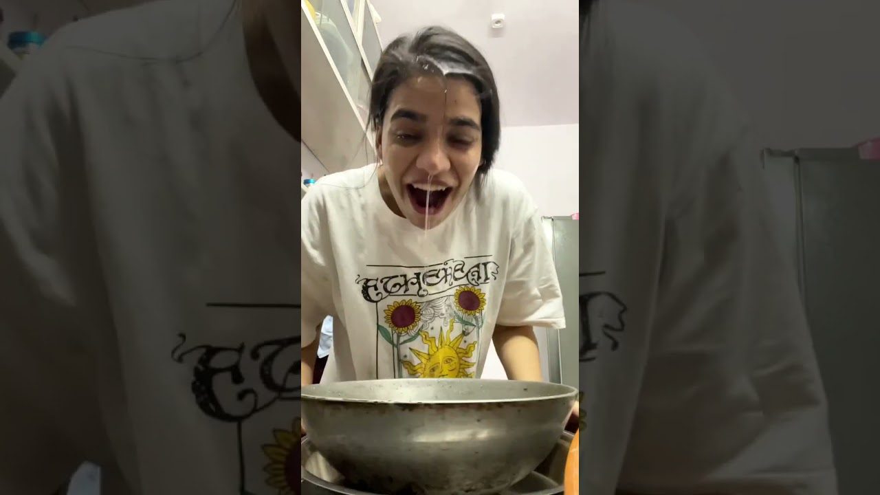 Jauna moteris linkstanti virš dubens, vandens lašai bėga per veidą, apsirengusi marškinėliais su saulės piešiniu