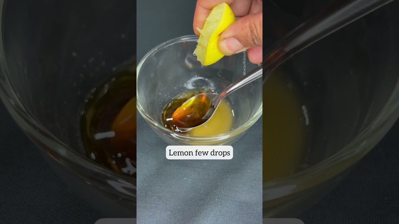 Rankos spaudžia citrinos griežinėlį virš indelio su medumi ir šaukštu.