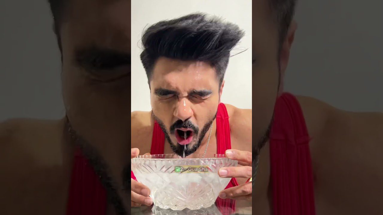 Vyras raudonai apsirengęs skalauja burną iš stiklinio dubens, vanduo tekėdamas iš burnos