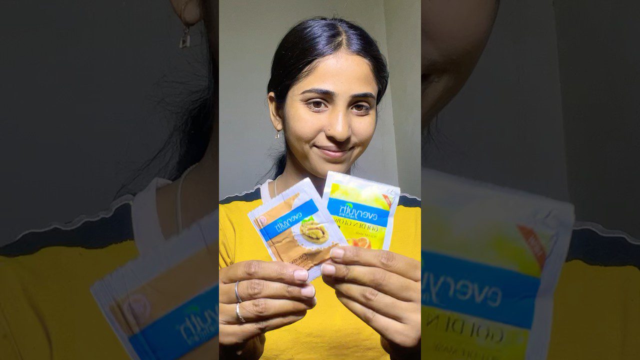 Jauna moteris geltonais marškinėliais laiko ir rodo dvi vienkartines arbatos pakelius (žolelių ir citrinos).