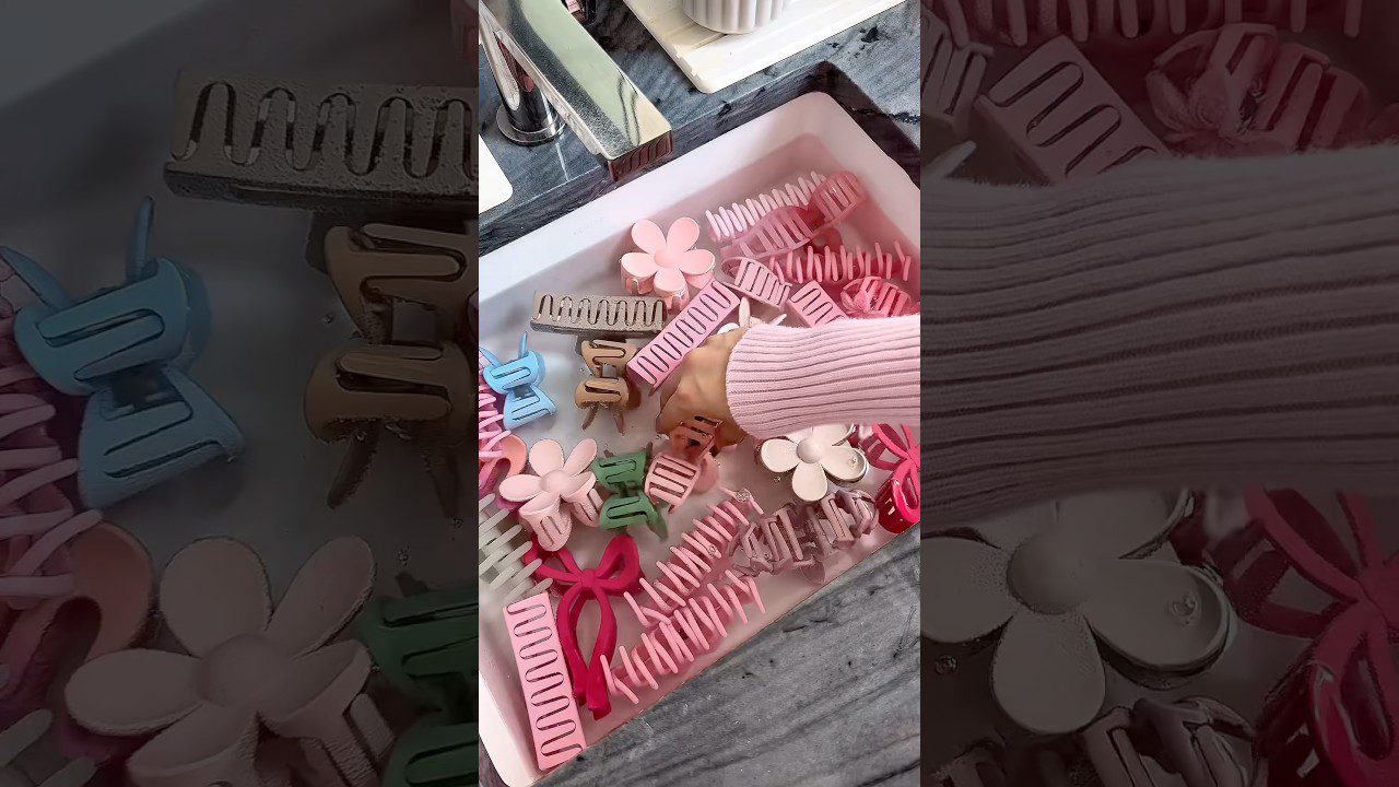 Ranka renka įvairias rožines, žalias ir mėlynas plaukų segtukes kriauklėje vandens.