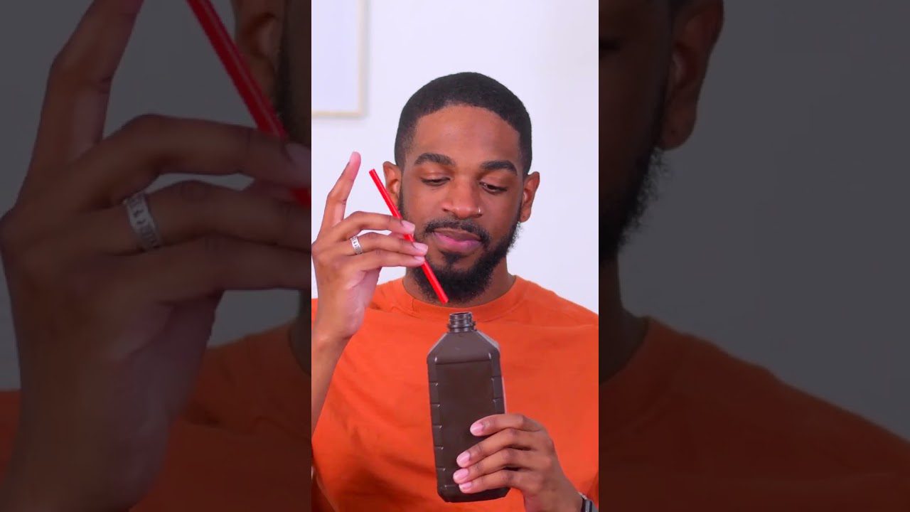 Vyras oranžiniais marškinėliais laiko juodą butelį ir įkiša raudoną šiaudelį