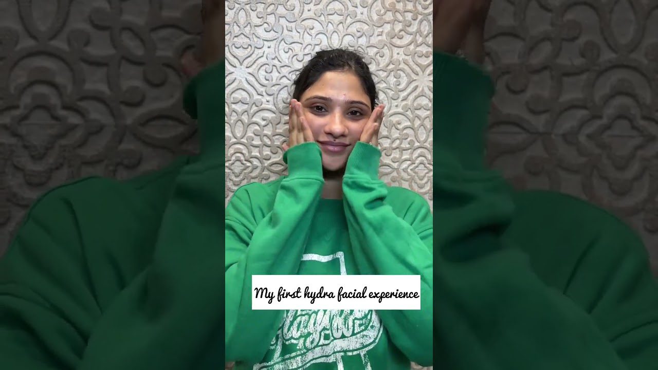 Moteris žaliai apsirengusi laiko veidą rankomis, užraše „Mano pirmoji hydra veido procedūra“