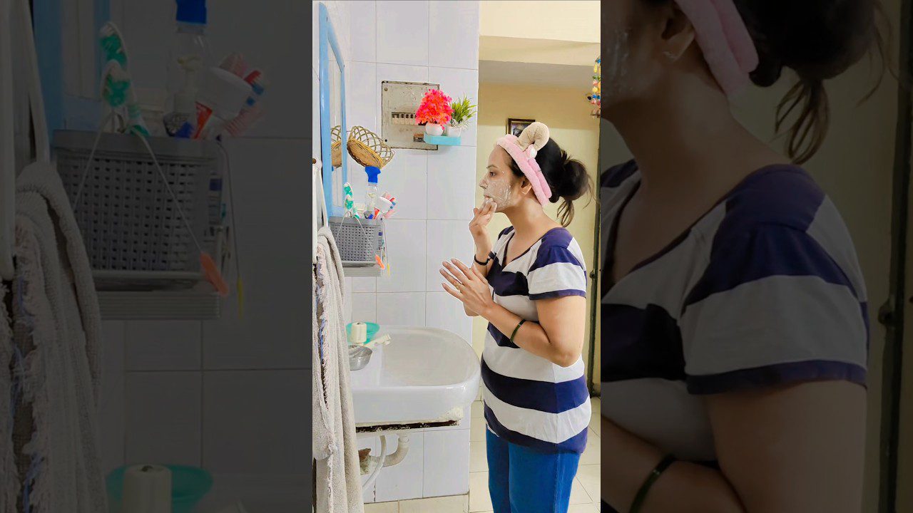 Moteris vonioje su kauke ant veido ir rožine galvos juosta žiūri į veidrodį