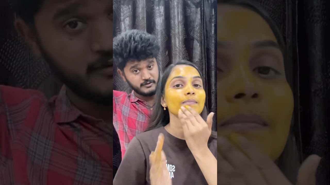 moteris tepasi geltoną veido kaukę, vyras stovi už jos, tamsi užuolaida fone