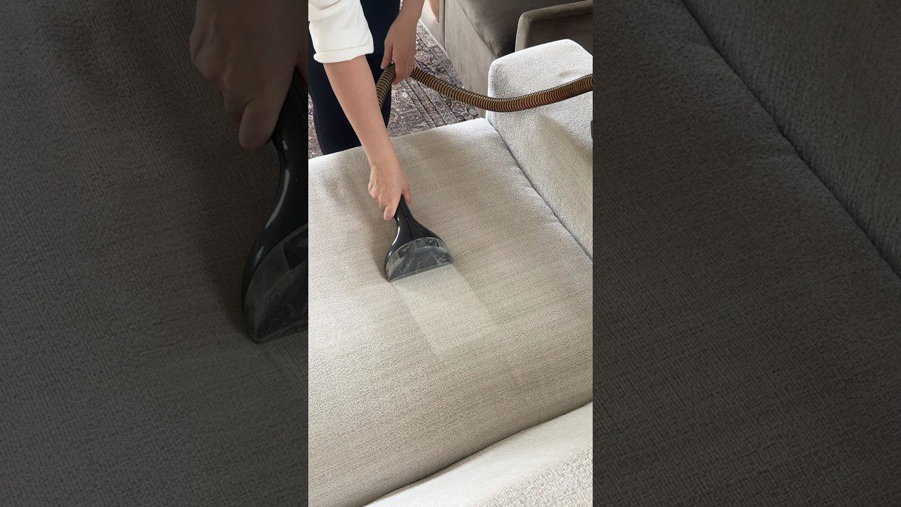 Rankus valomas dulkių siurbliu ant šviesios sofų sėdynės, matomas valymo rezultatas