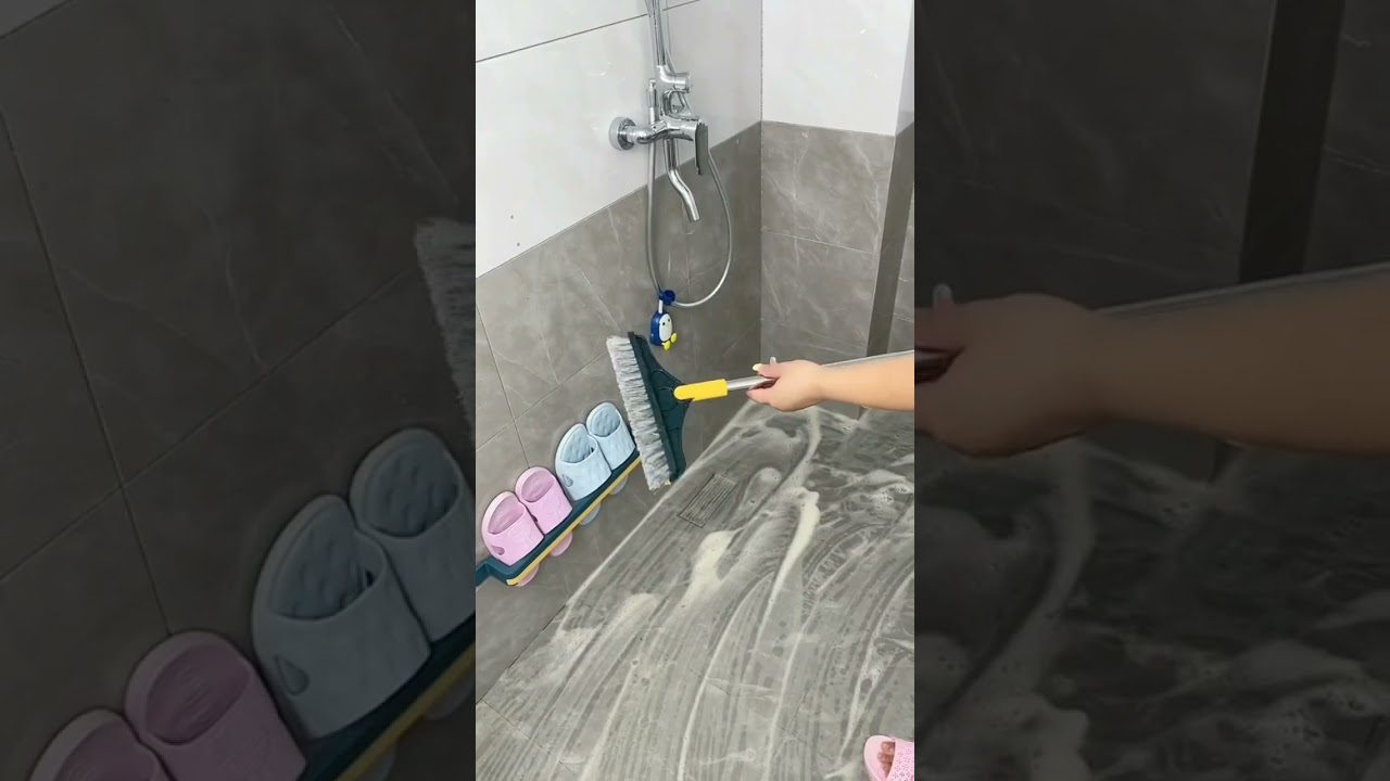 Rankos šepetys plauna putotas grindis duše, šalia pakabintos šlepetės ir žaislo.