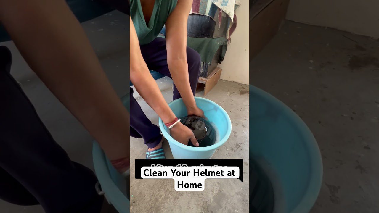 Žmogus rankomis plauna motociklo šalmo vidų mėlyname kibire su vandeniu.
