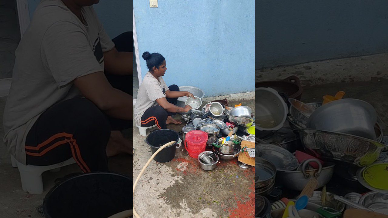 Moteris plauna daug virtuvės indų ant žemės prie mėlynos sienos ir kibiro.