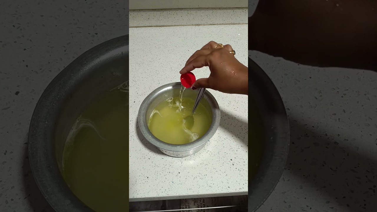 Rankos pilsto skaidrų skystį iš raudono kamštelio į metalinį indą su geltonu skysčiu ir šaukštu.