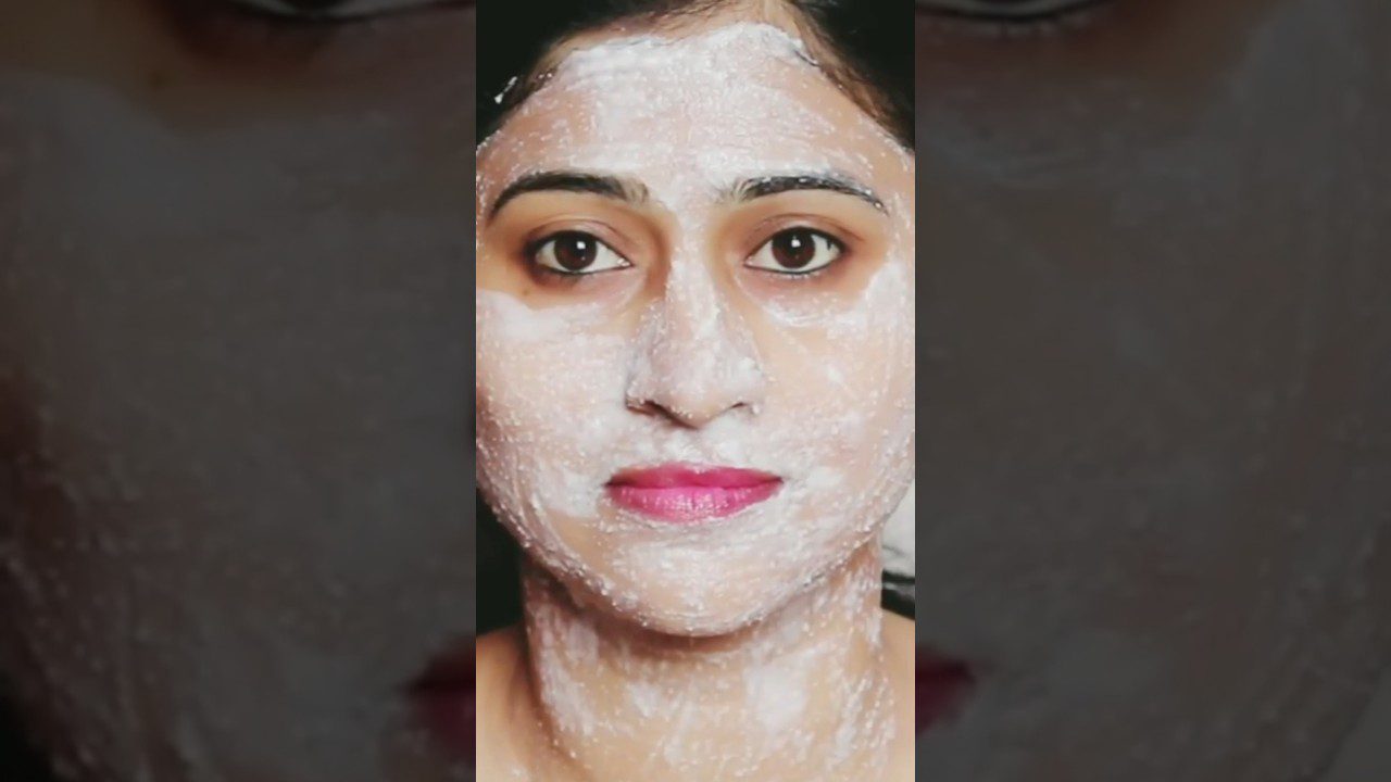 Moteris su balta veido kauke ir ryškiomis rožinėmis lūpomis, žvelgia tiesiai į priekį