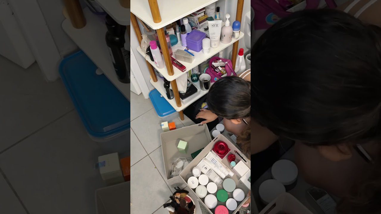 Moteris susirinkinėja kosmetiką ir priežiūros priemones iš lentynos ir dėžių.