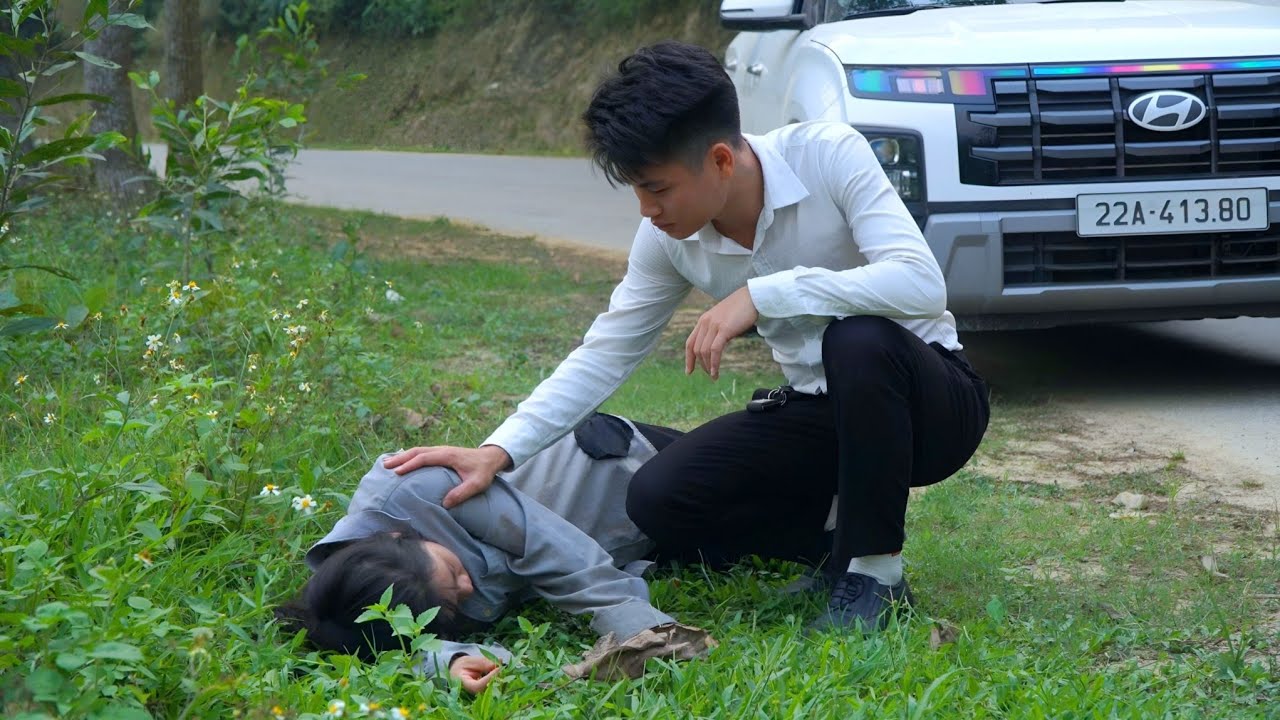 Jaunuolis patikrina ant žolės gulinčią moterį šalia sustojusio automobilio.