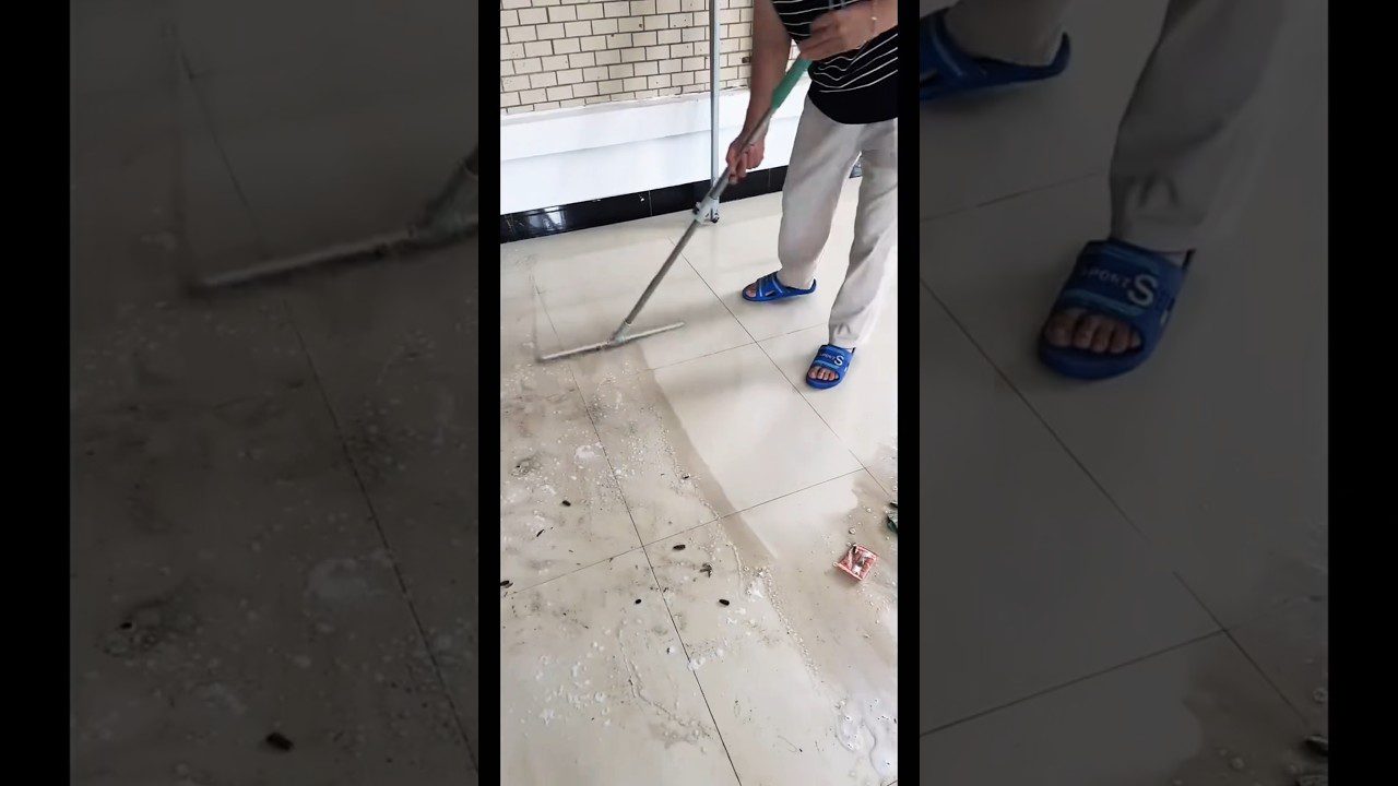 Vyras vilki mėlynas šlepetes ir stumia šluotą per nešvarius, šlapius plytelių grindis