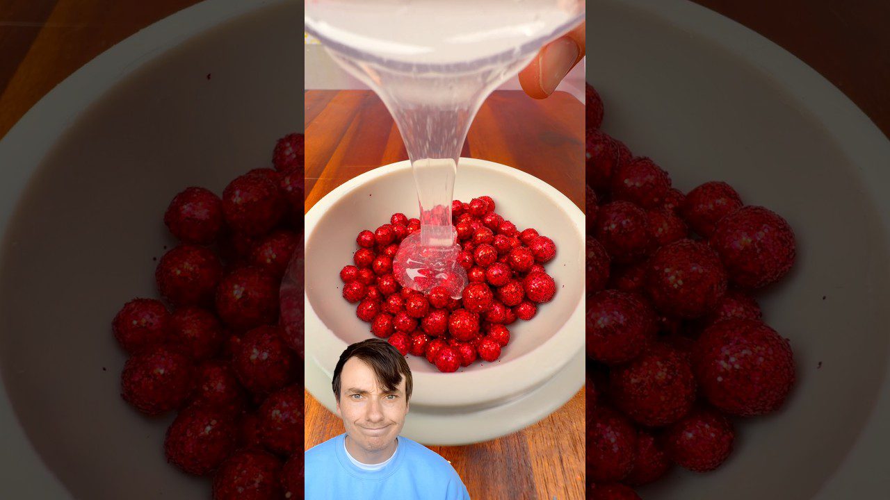 Baltoje lėkštėje raudonos blizgios saldainių rutuliukai, ant jų pila permatomą želę