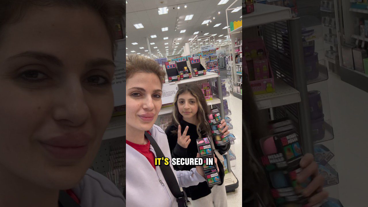 Motina ir dukra parduotuvėje laiko žaislų paketus, dukra rodo V ženklą.