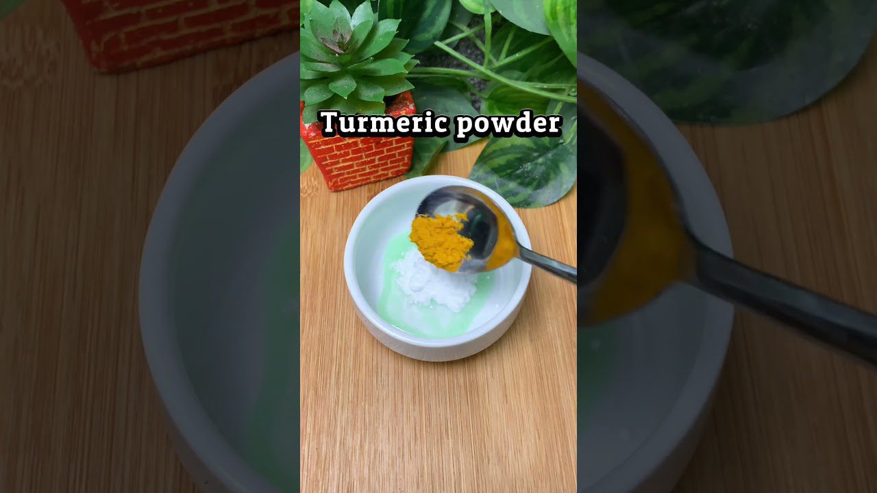 Šaukštas ciberžolės krenta ant baltos indelio su balta pasta ir žalsvu skysčiu.