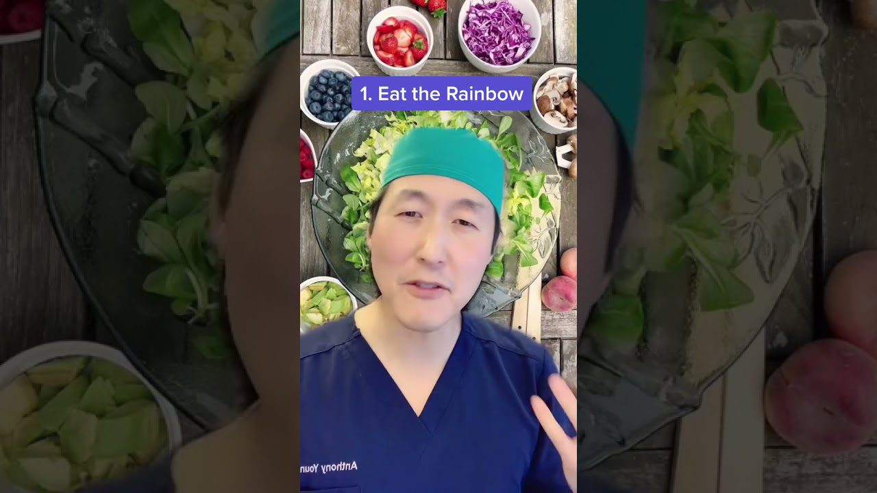 Vyras medicininiais drabužiais kalba priešais lėkštę salotų ir užrašu „Eat the Rainbow“