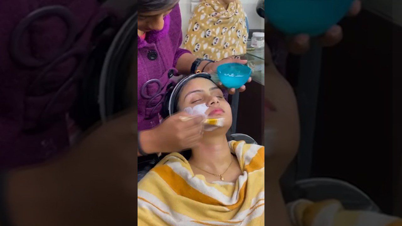 Moteris atsigulusi su uždėtu rankšluosčiu, jai kosmetologė tepasi veidą kauke.