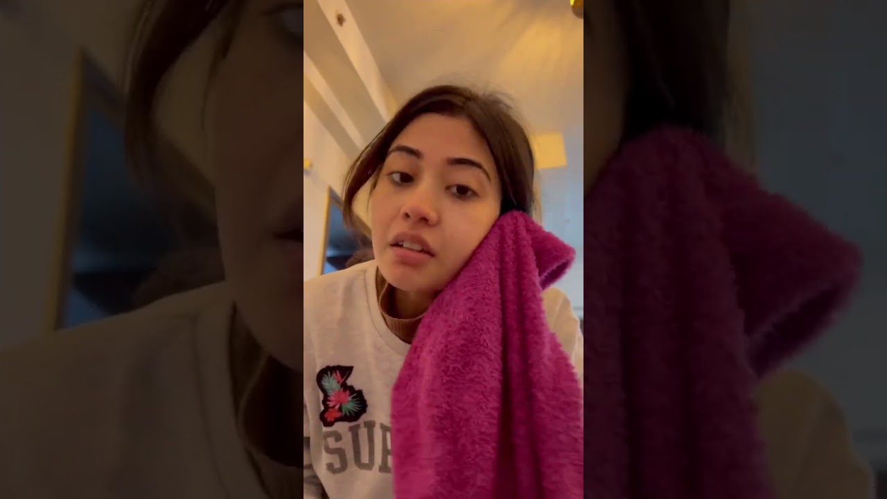 Jauna moteris ranka priglaudusi ryškiai rožinį rankšluostį prie skruosto, namų aplinka