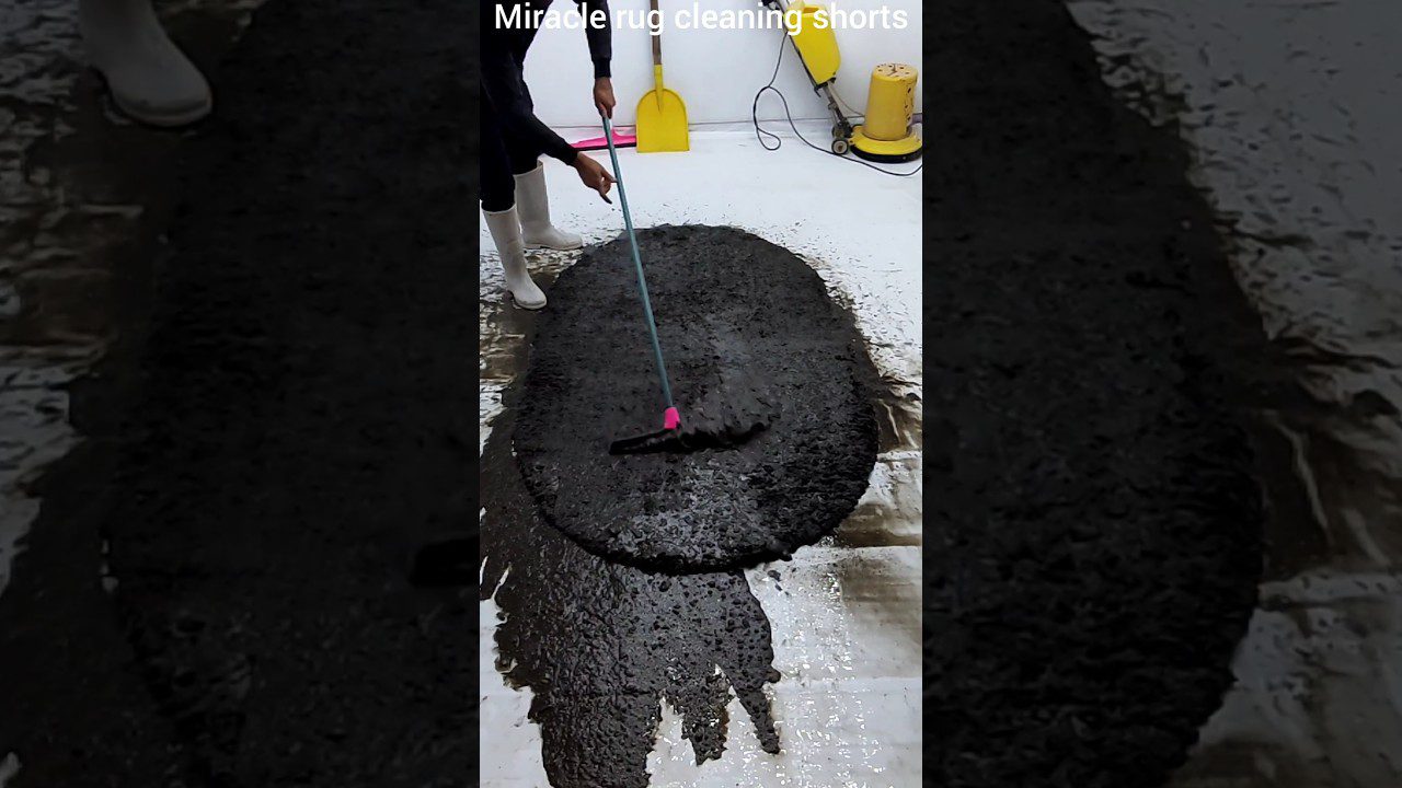 Žmogus su baltomis gumines batais braukia šepečiu didelį juodą tepalinį dėmę ant baltos grindų dangos