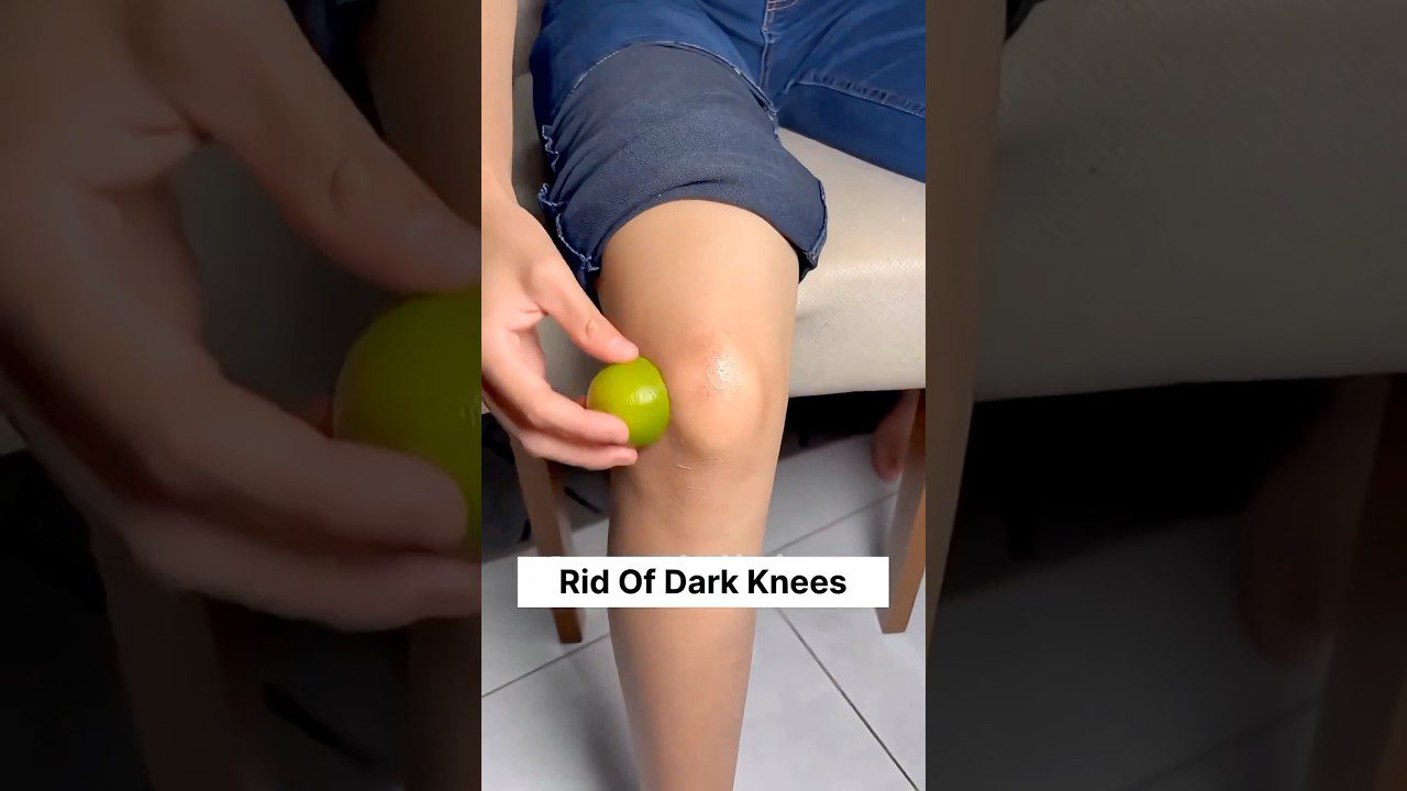 Rankos trina žalią citriną ant kelių šalia užrašo „Rid Of Dark Knees“