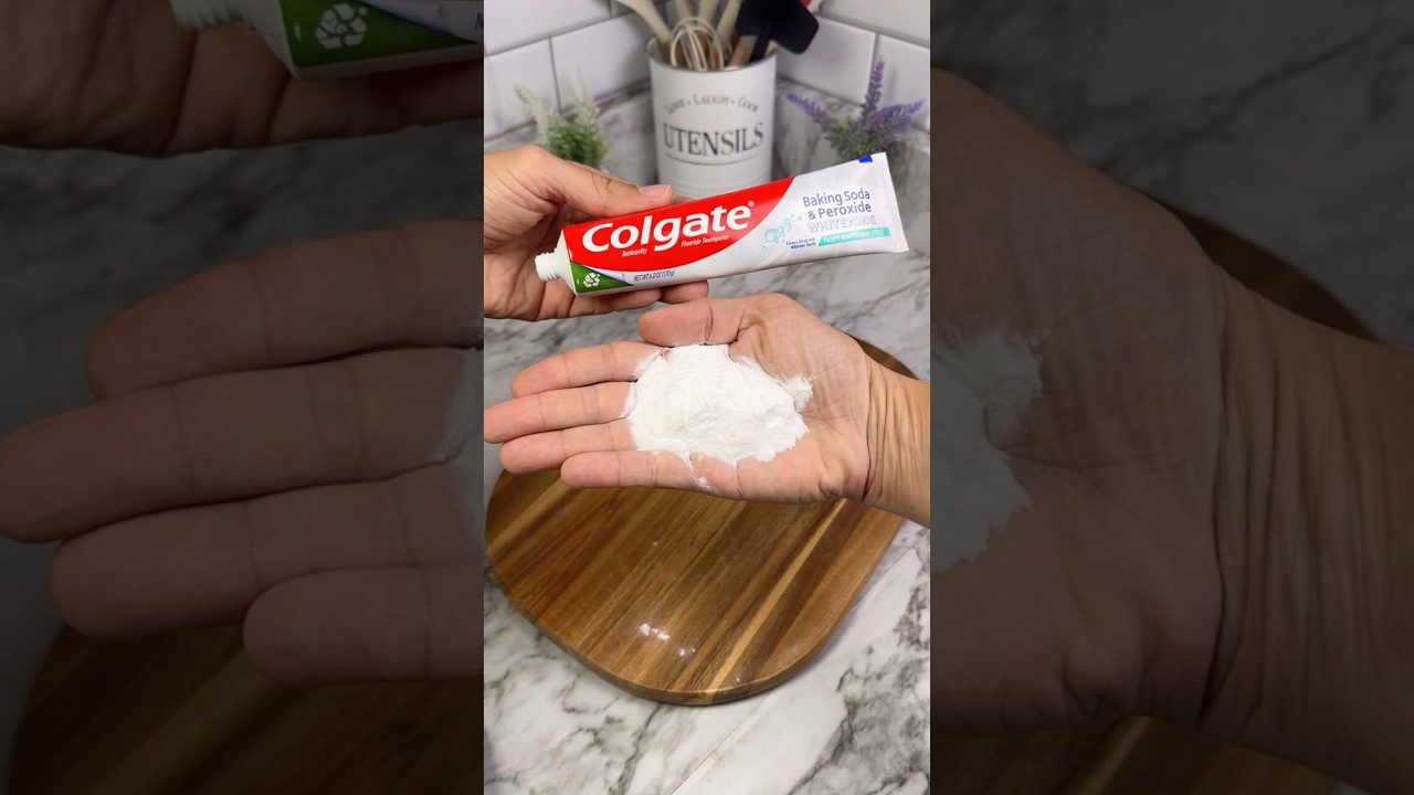 Rankų delne baltas miltelis ir išspaustas Colgate dantų pastos tūbelė su užrašu „Baking Soda & Peroxide“.
