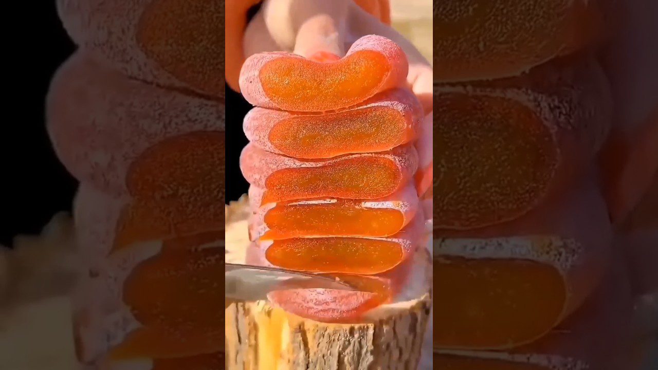 Rankomis supjaustytos oranžinės želė juostelės apibarstytos cukraus dulkėmis ant medžio.