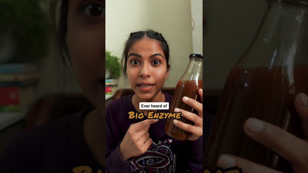Jauna moteris laiko stiklainiuką su tamsiu skysčiu ir klausia apie biofermentą