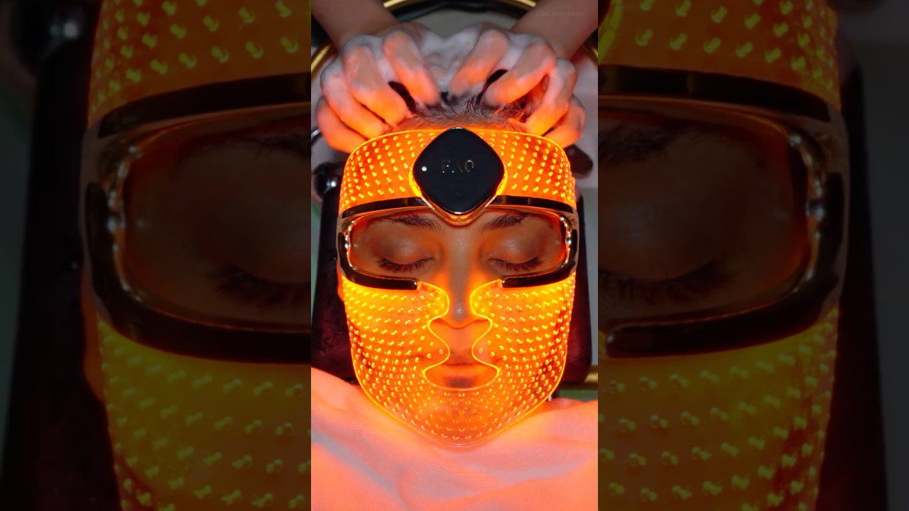 Moteris guli su užmerktomis akimis, ant veido ryškiai oranžinė LED šviesos terapijos kaukė