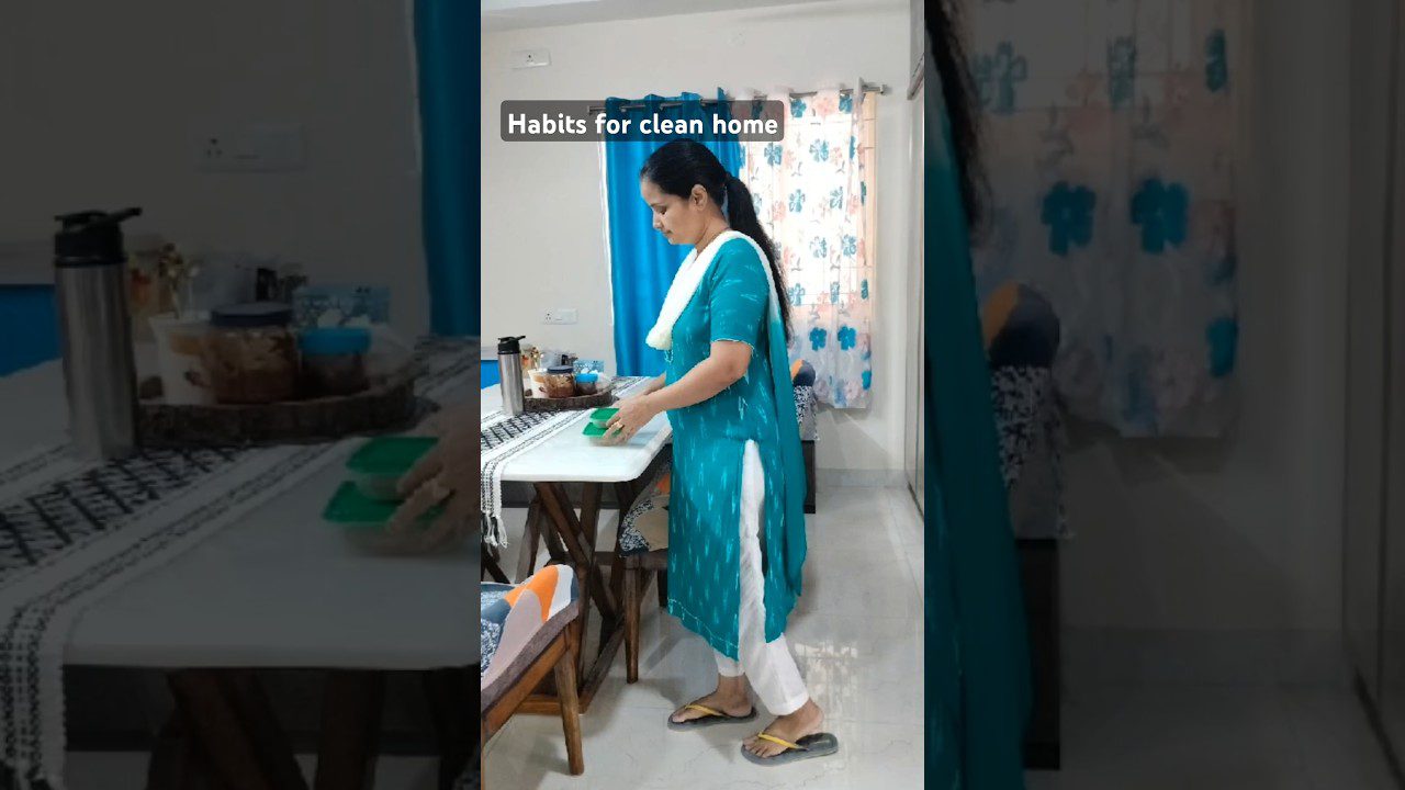 Moteris mėlyname chalate valanti stalą su kempine, ant stalo indai ir termosas