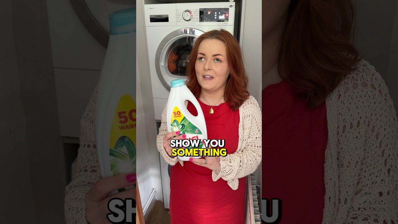 Moteris raudonomis suknelėmis laiko skalbiklių butelį prie skalbimo mašinos, tekstas „SHOW YOU SOMETHING“