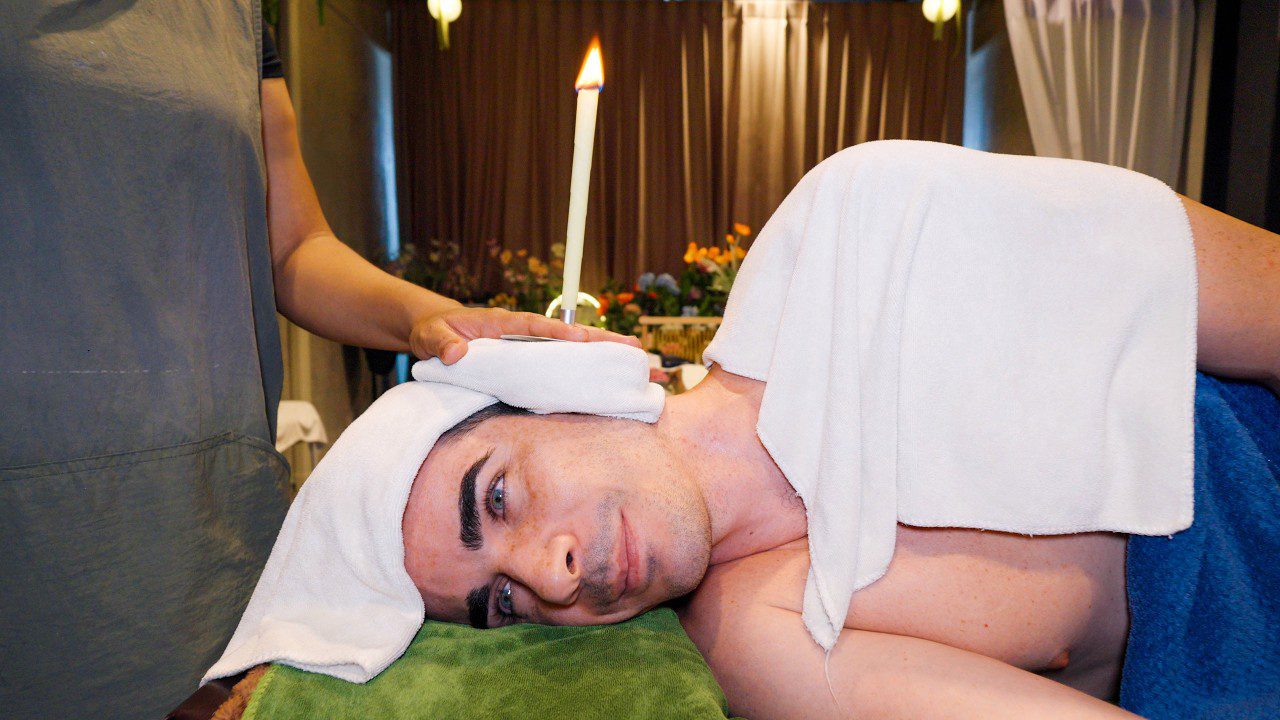 Vyras gulintis ant šono su estetiko uždėtomis rankšluostėmis ir degančia ausų žvakele