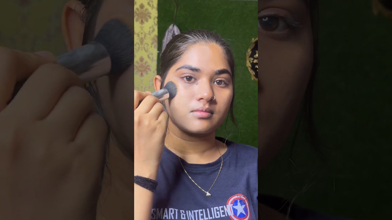 Jauna moteris tepasi skaistalus šepetėliu, matomas nosies žiedas ir marškinėliai.