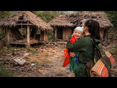 Moteris laiko besišypsantį vaiką prie kaimiškų nendrių pastogių ir šiukšlų.