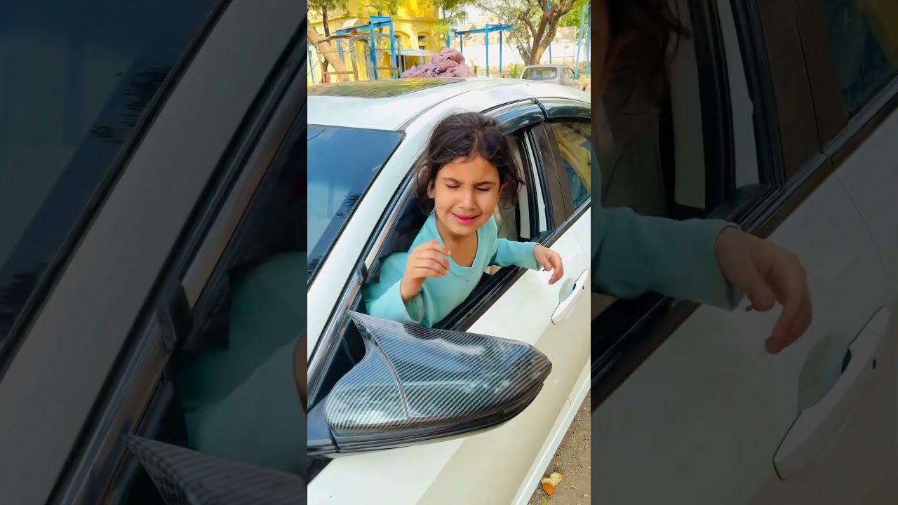 Mergaitė išlindusi pro automobilio langą šypsosi ir tiesia ranką į priekį.