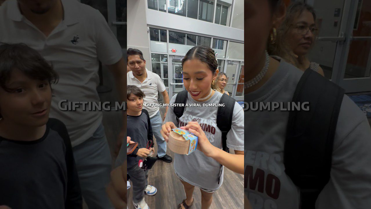 Jauna moteris priima mažą dovaną dėžutėje, aplink stovi šeimos nariai.