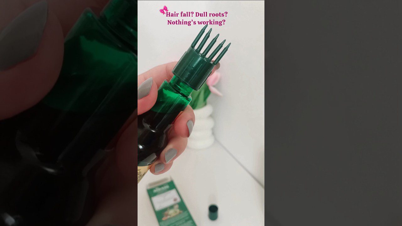 Rankoje laikomas žalias plaukų priežiūros buteliukas su masažiniu šukų antgaliu.