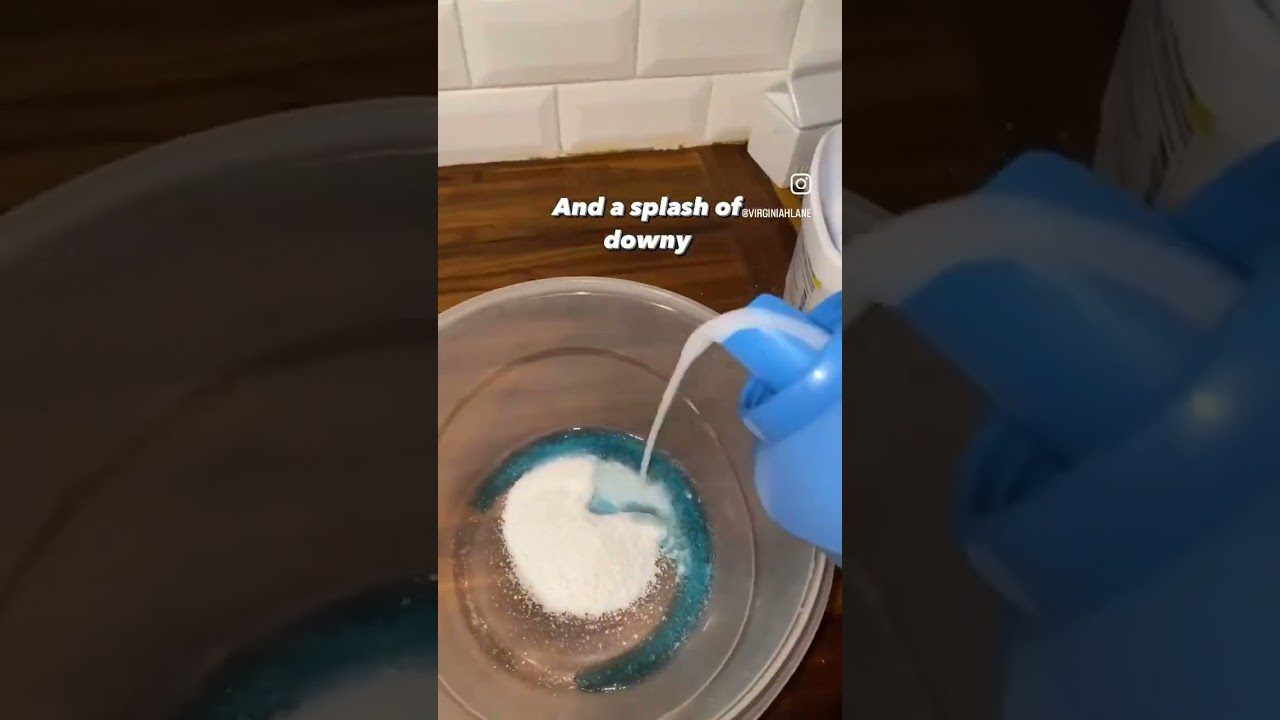 Mėlynas skalbimo skystis ir balti milteliai pilami į permatomą dubenį virtuvėje