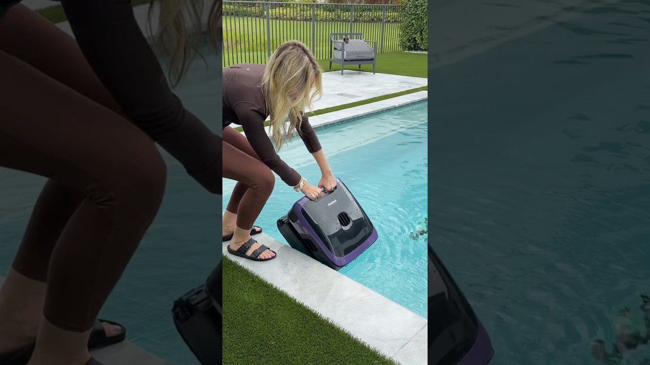 Moteris prileidžia automatinį baseino siurblį į skaidrų lauko baseino vandenį.