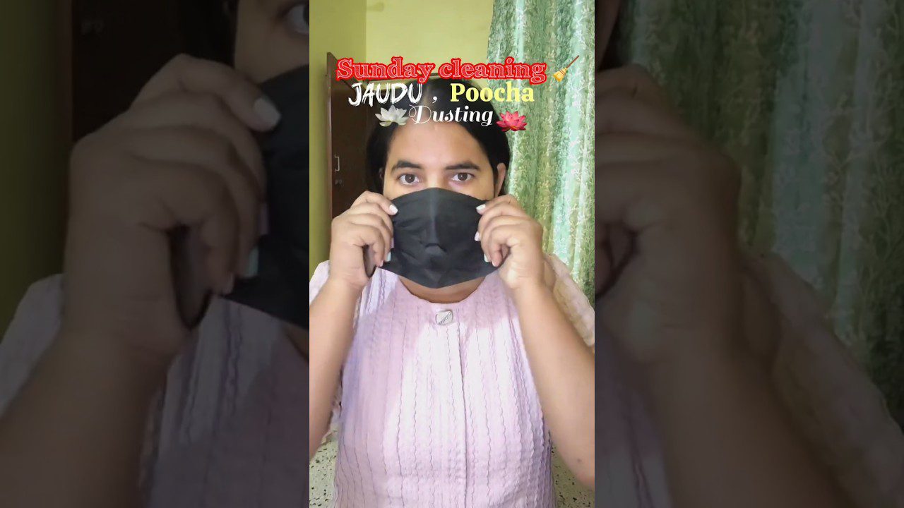 Moteris dėvi juodą apsauginę kaukę namų fone, viršuje užrašas „Sunday cleaning“