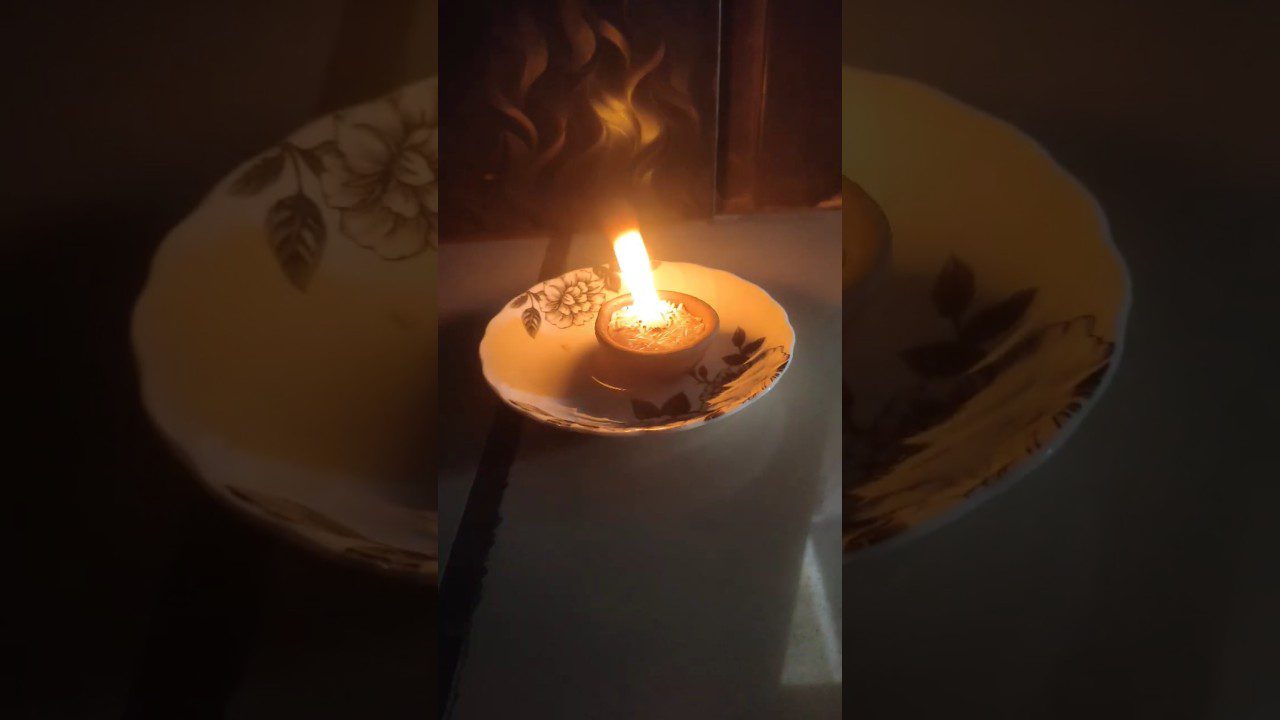 Deganti žvakė mažame indelyje ant dekoruoto porcelianinio lėkštutės.