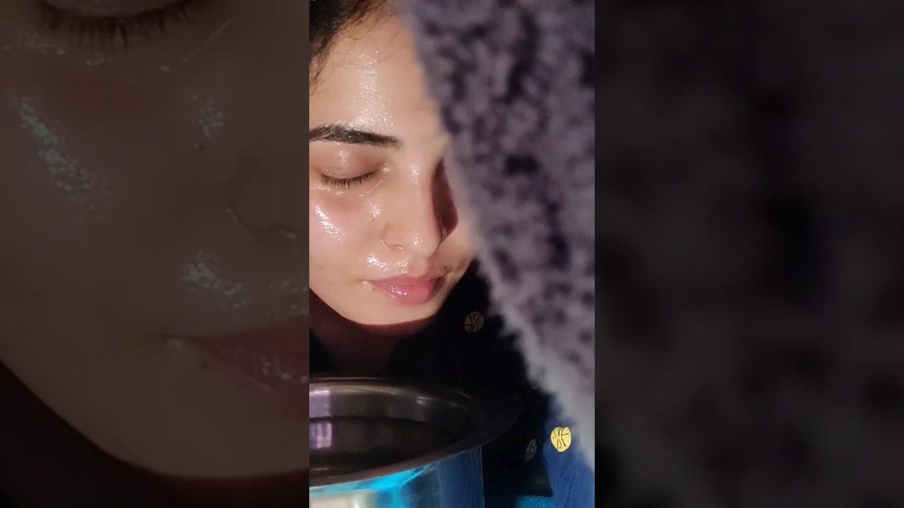 Moteris su užmerktomis akimis garinasi virš metalinio indelio su vandeniu.