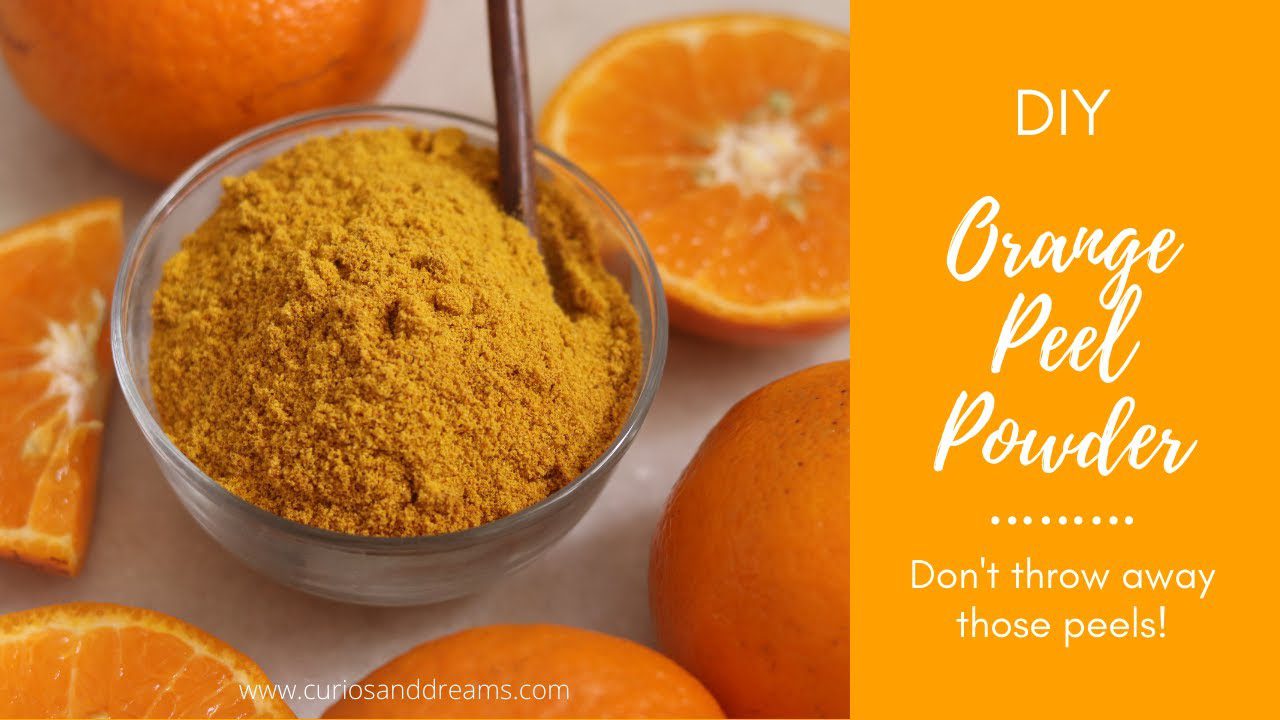 Stiklinė dubenė su smulkiu oranžiniu žievelių milteliais ir apkirptos mandarinų skiltelės, užrašas „Orange Peel Powder“ (apelsinų žievelių milteliai)