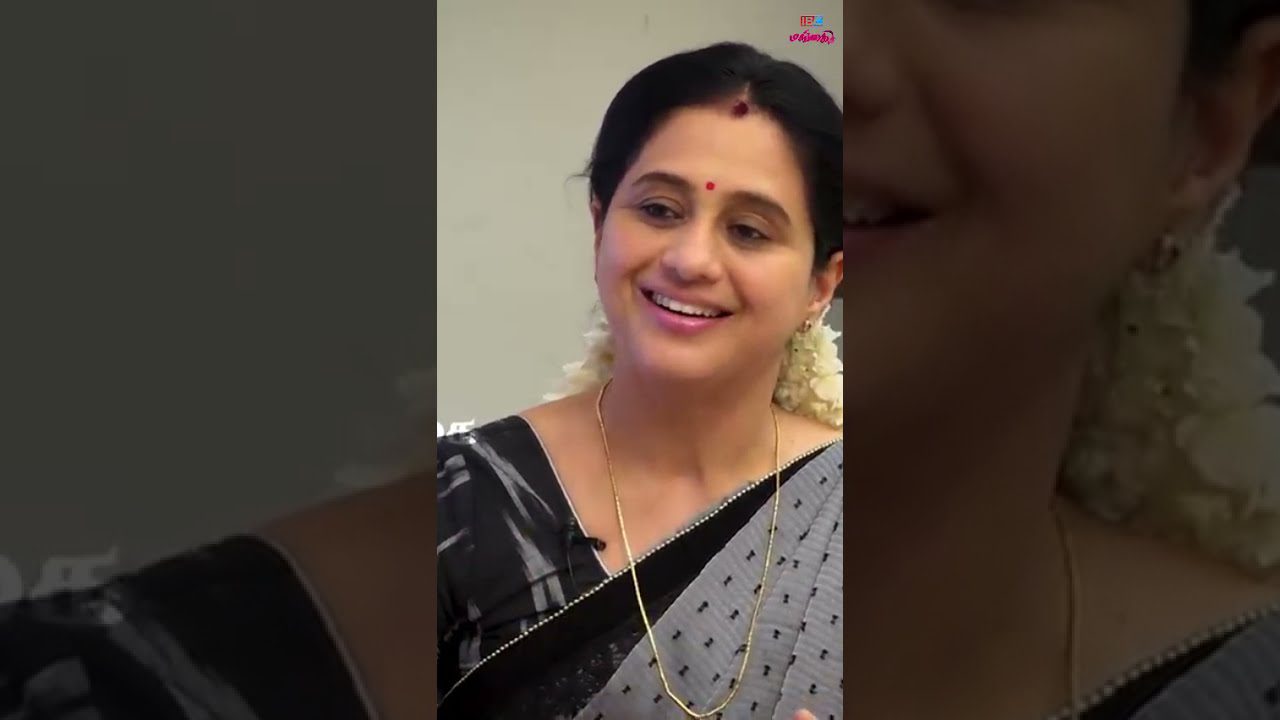 Indiška moteris su juoda‑pilka saree, gėlėmis plaukuose ir raudonu bindi ant kaktos, šypsosi