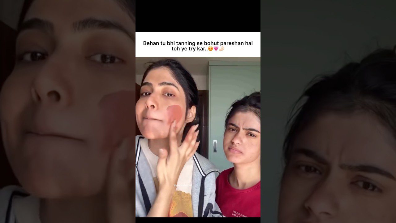 Dvi jaunos moterys: viena tepasi raudoną kaukę ant skruosto, kita stebisi fone, viršuje užrašas hindi kalba.